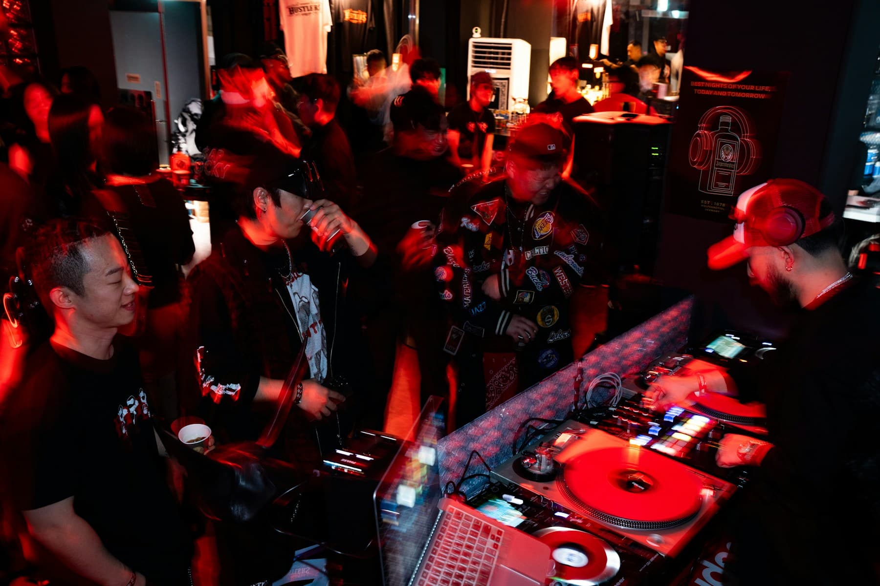 People gathered around a DJ booth at a club under red light