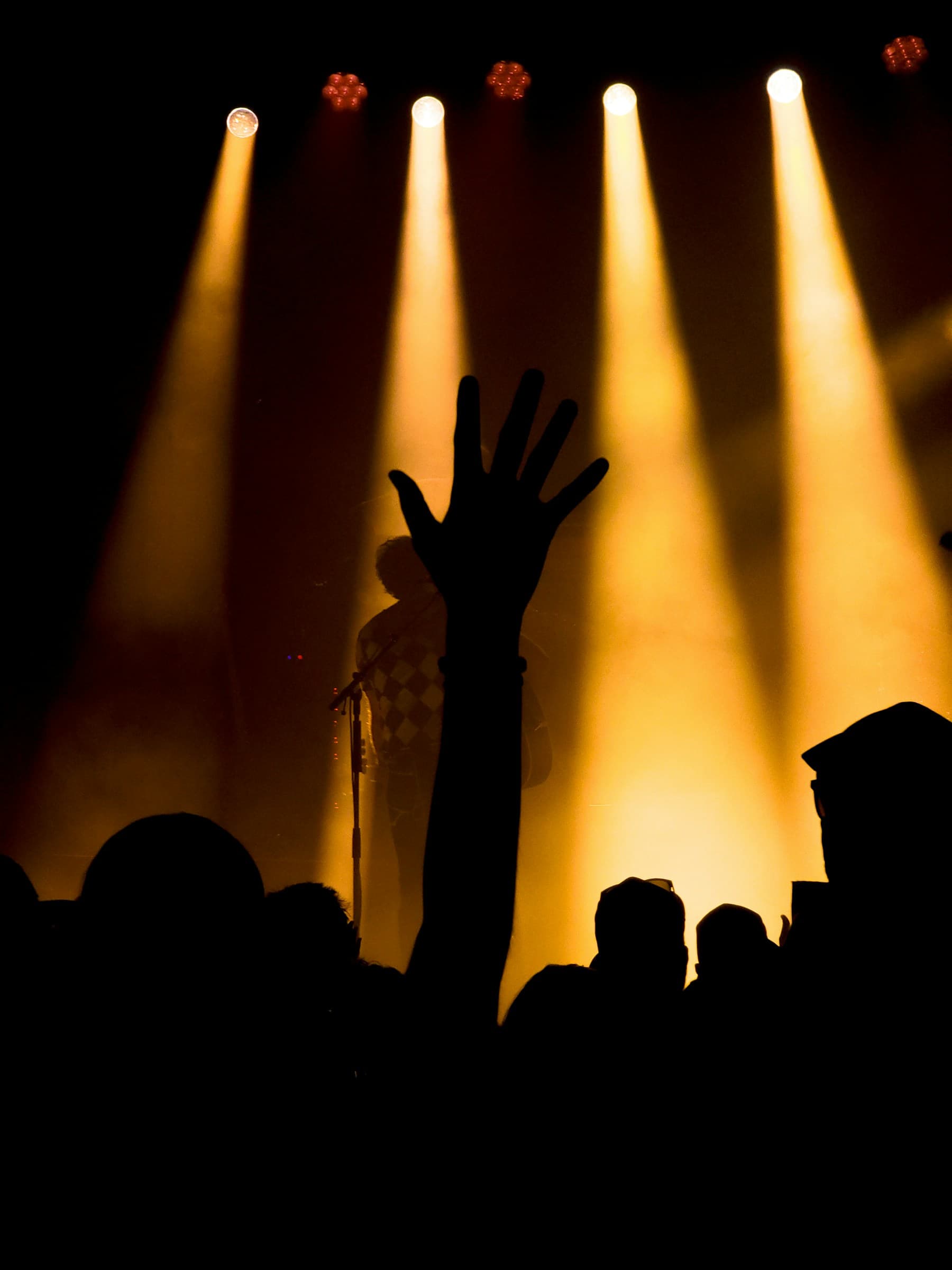 A concert crowd with hands raised under stage lights