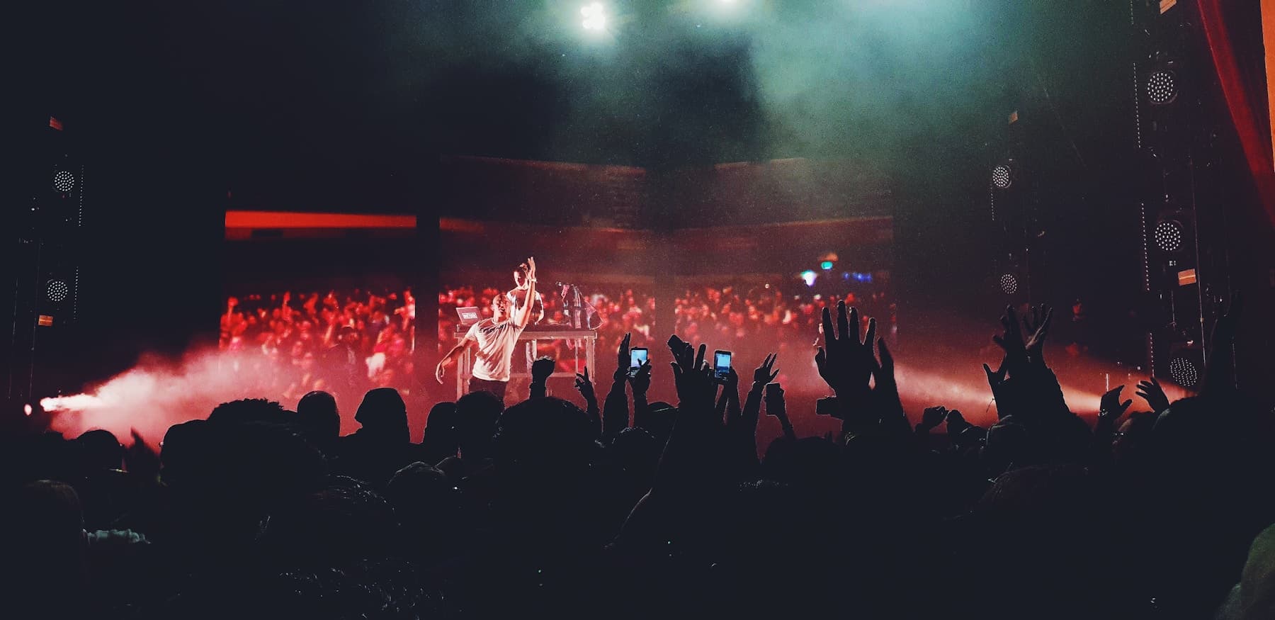 People raising their hands in front of a stage filled with smoke